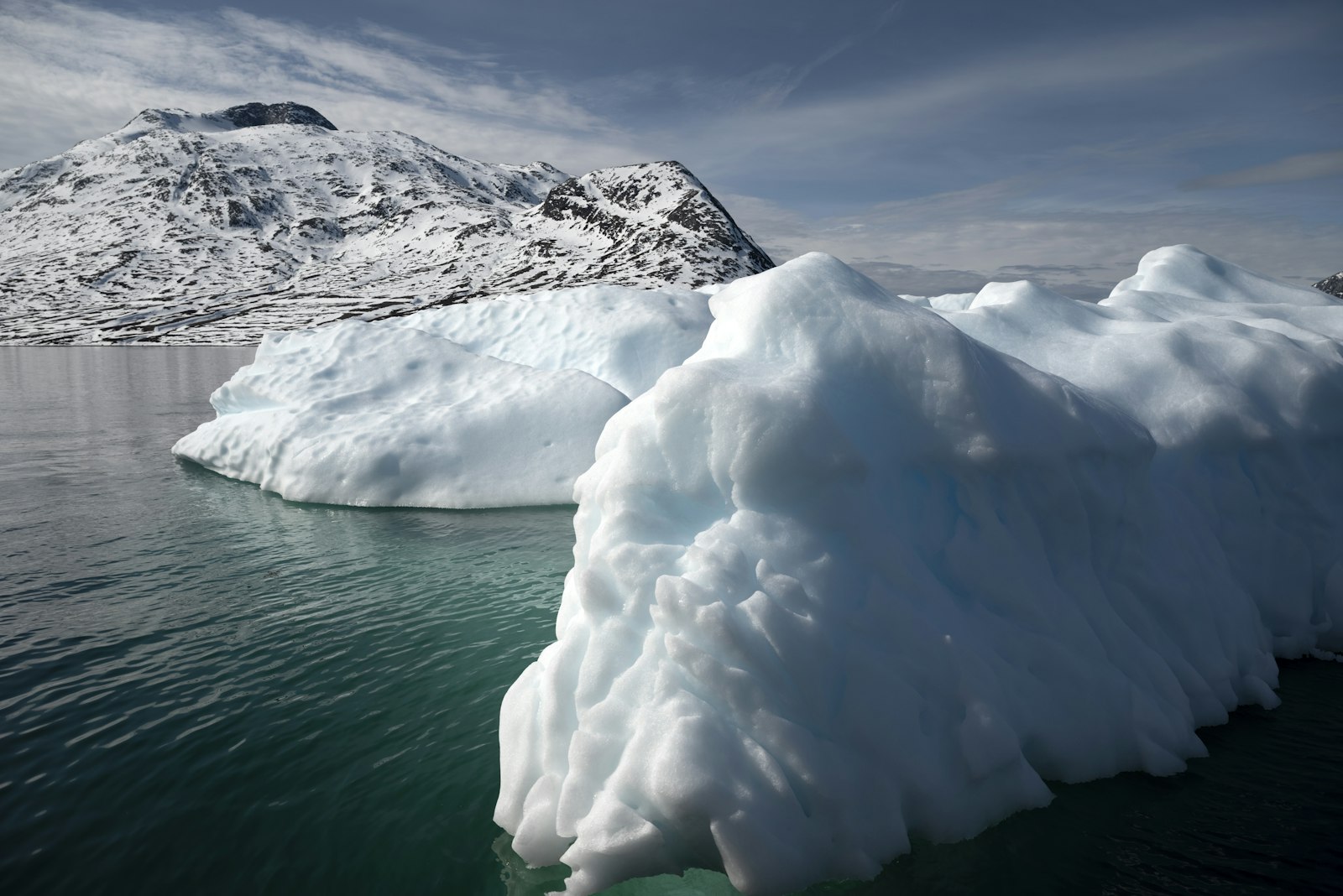 Large white icebergs in a calm bay backed by snow-capped mountains